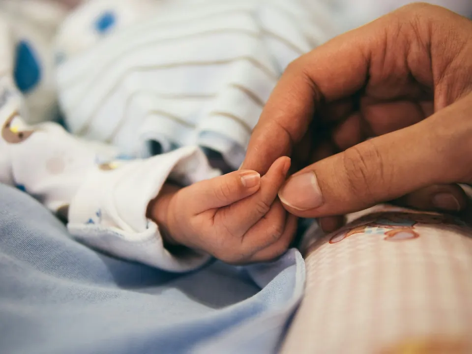 A newborn baby's hand holding a parent's finger