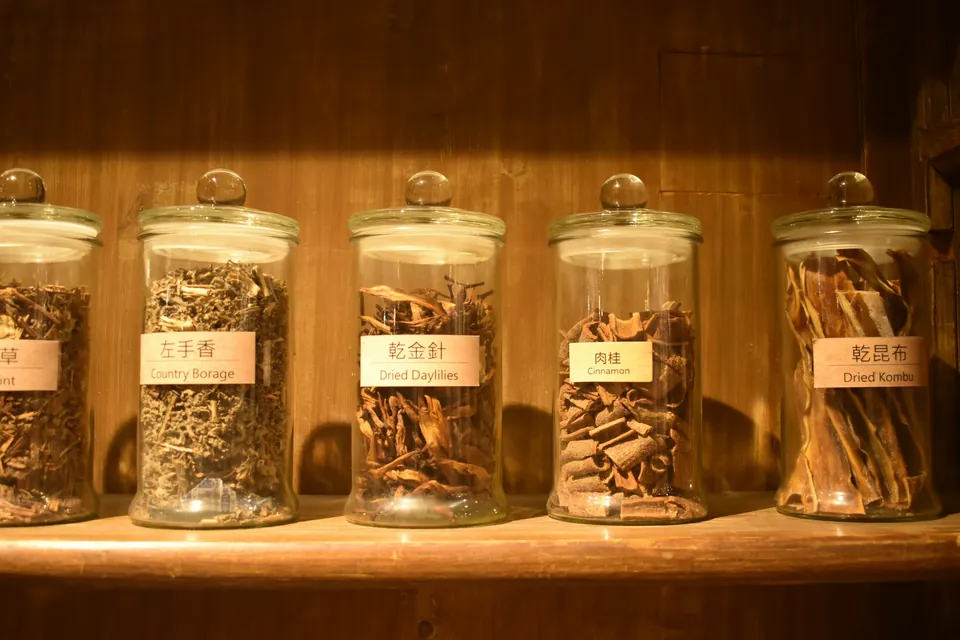 Glass jars of dried herbs used in traditional Chinese medicine on a wooden shelf
